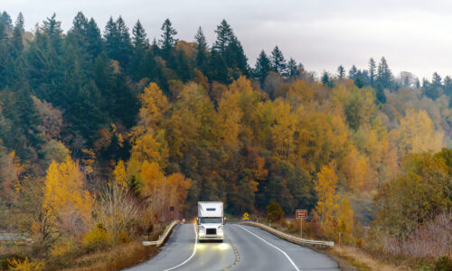 White big rig semi truck transporting goods on the winding autum